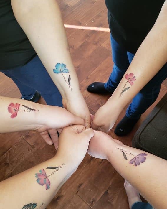 Four hands displaying matching flower tattoos with different colored petals blue, pink, red